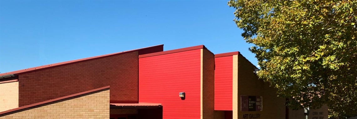 Outside of the Cowra Regional Art Gallery, showing red panelling, roof and green tree.