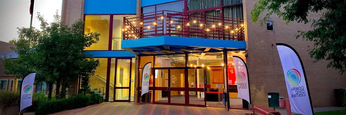 Exterior of the Cowra Civic Centre at dusk, with flags out and lights on.